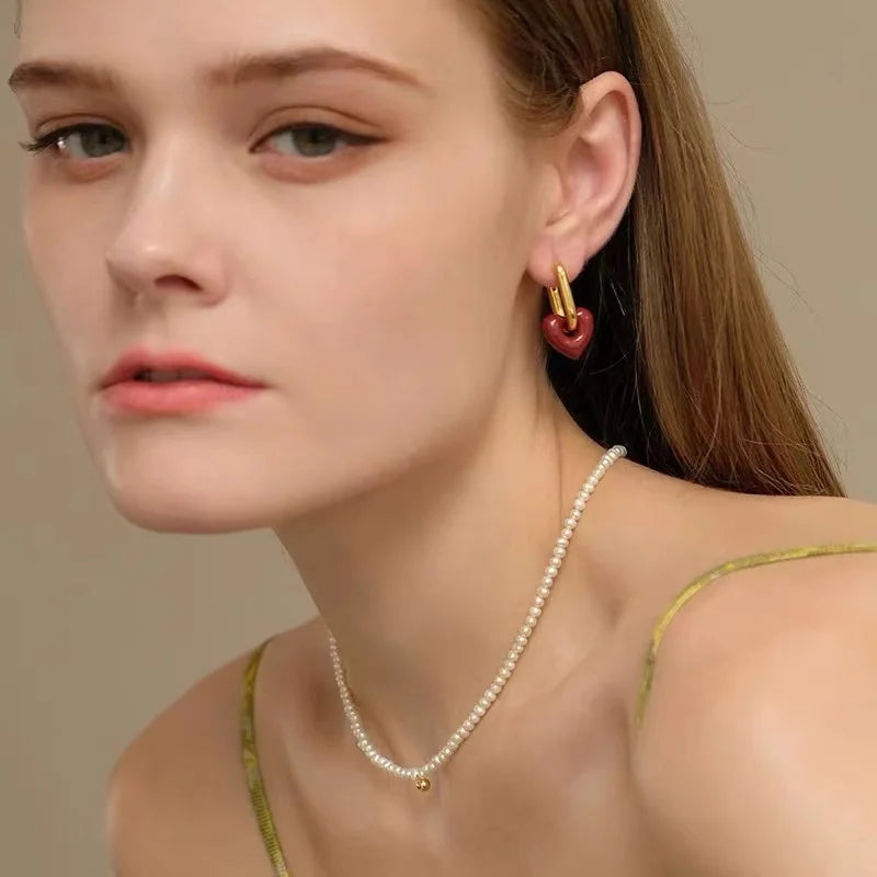Close-up of a woman wearing heart-shaped earrings and a pearl necklace against a neutral background
