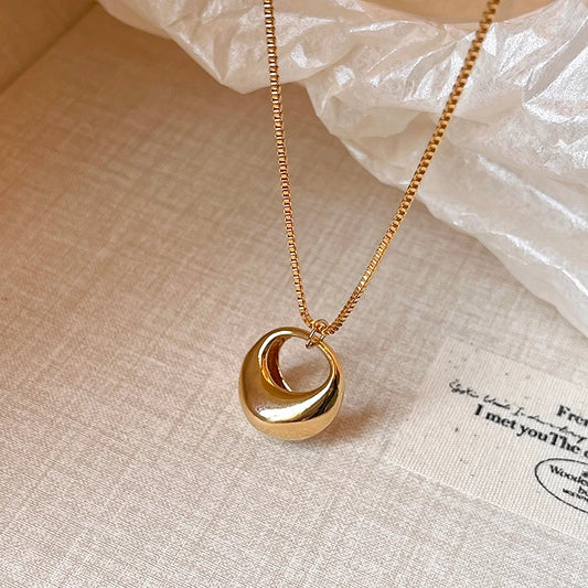 Gold necklace with a unique pendant on a textured beige surface