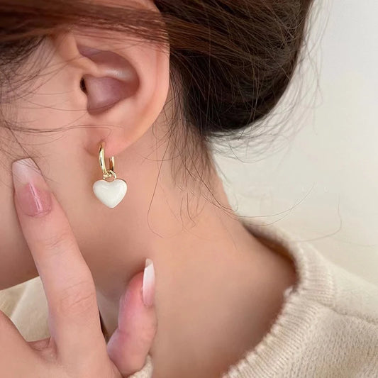 Close-up of a person wearing a gold earring with a heart-shaped white charm.