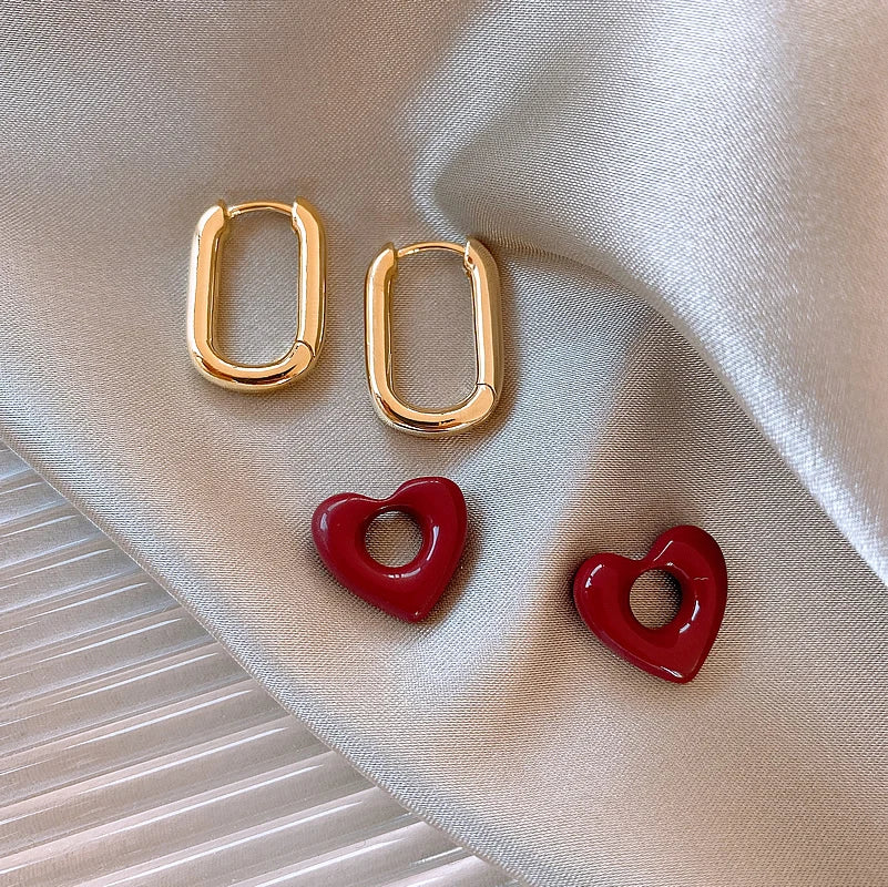 Gold hoop earrings with red heart-shaped pendants on a beige fabric background