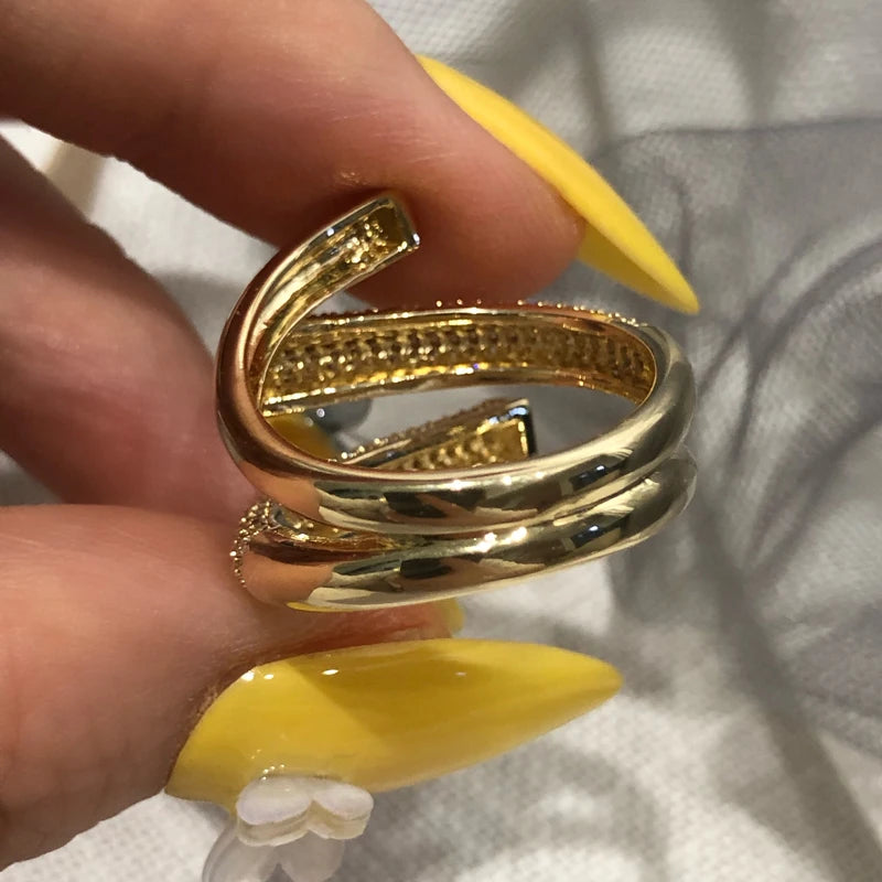 Gold spiral ring held by a hand with yellow nail polish on a neutral background