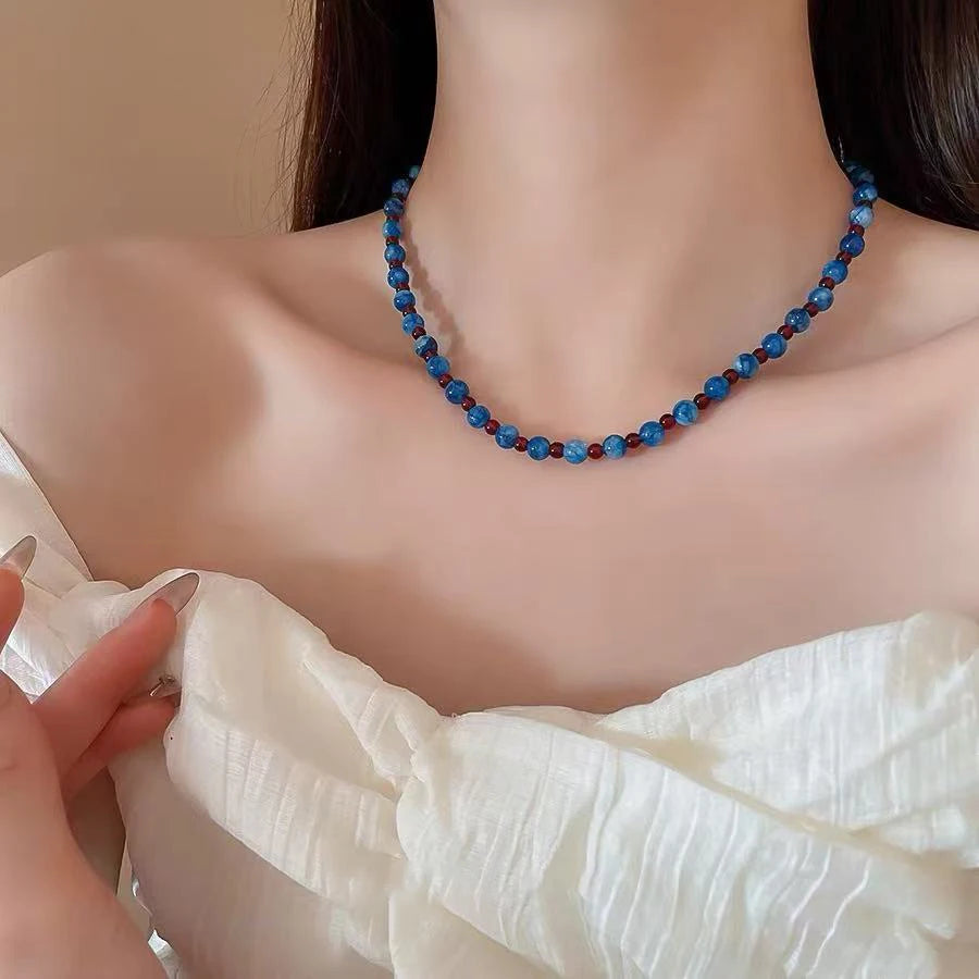 Necklace with blue and red beads worn by a person against a neutral background