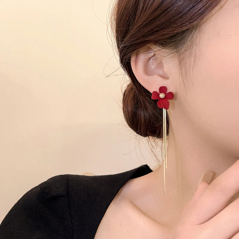Red floral earring worn by a person on a beige background