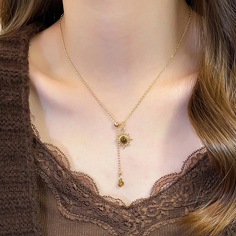 Gold necklace with a sun pendant worn by a person with brown hair and a brown top.