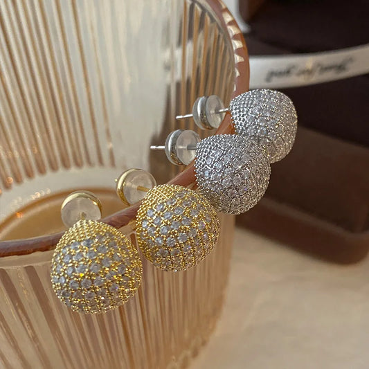 Gold and silver ball-shaped earrings on a wooden stand.