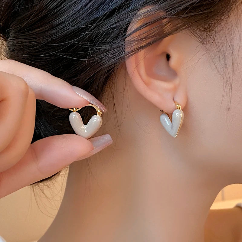 Close-up of a person wearing heart-shaped earrings with a hand adjusting one of them.
