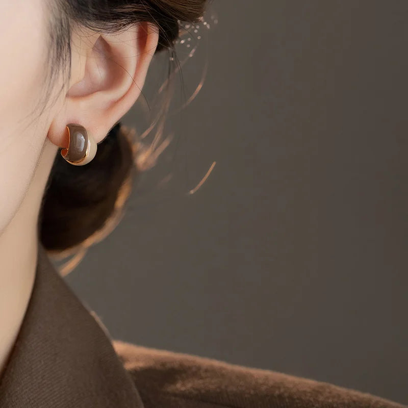 Close-up of an ear wearing a brown earring against a neutral background