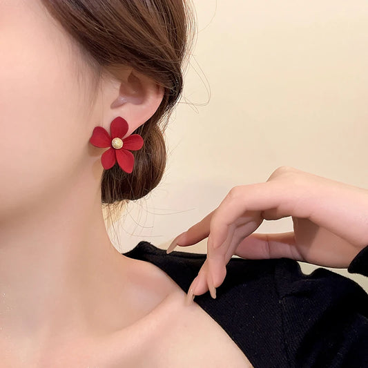 Red flower-shaped earring worn by a person with a neutral background