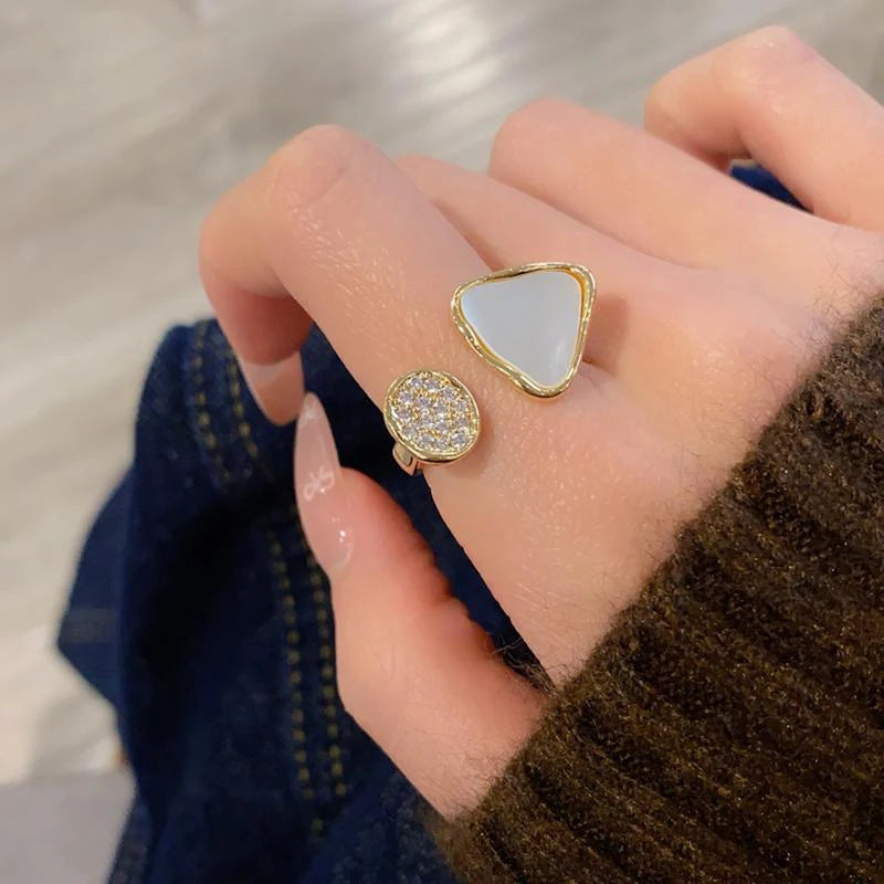 Hand wearing two gold rings with different designs on a neutral background