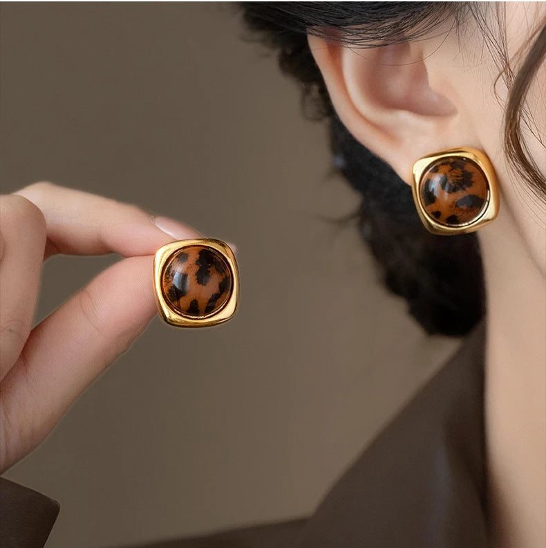 Gold earrings with leopard print design worn by a person against a neutral background