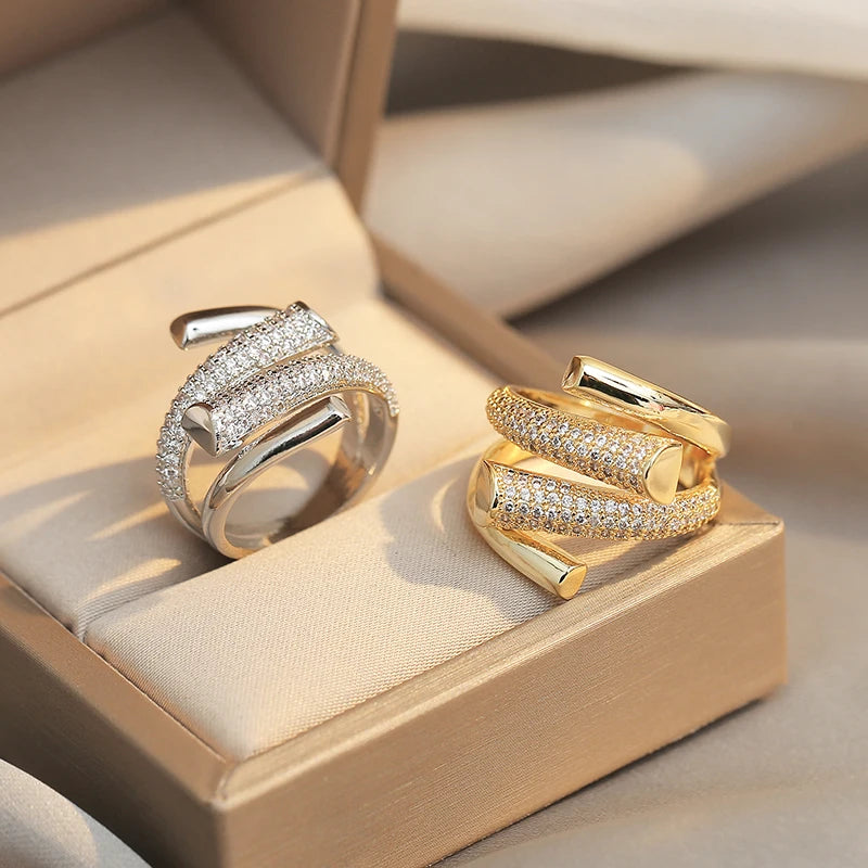 Two gold rings with diamond accents on a beige cushion in a box.
