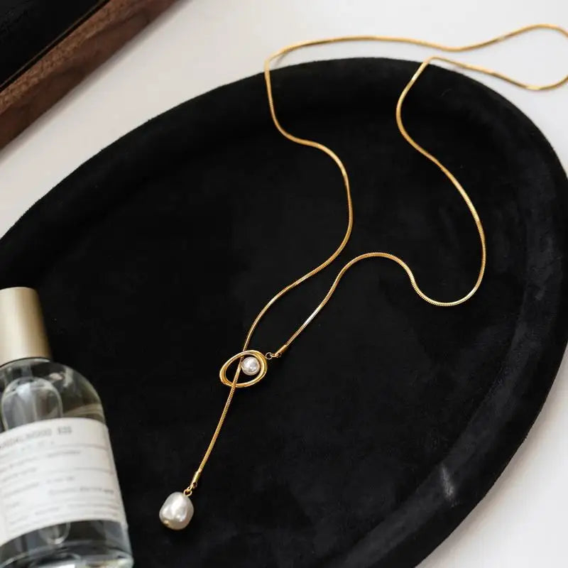 Gold necklace with a pearl pendant on a black tray