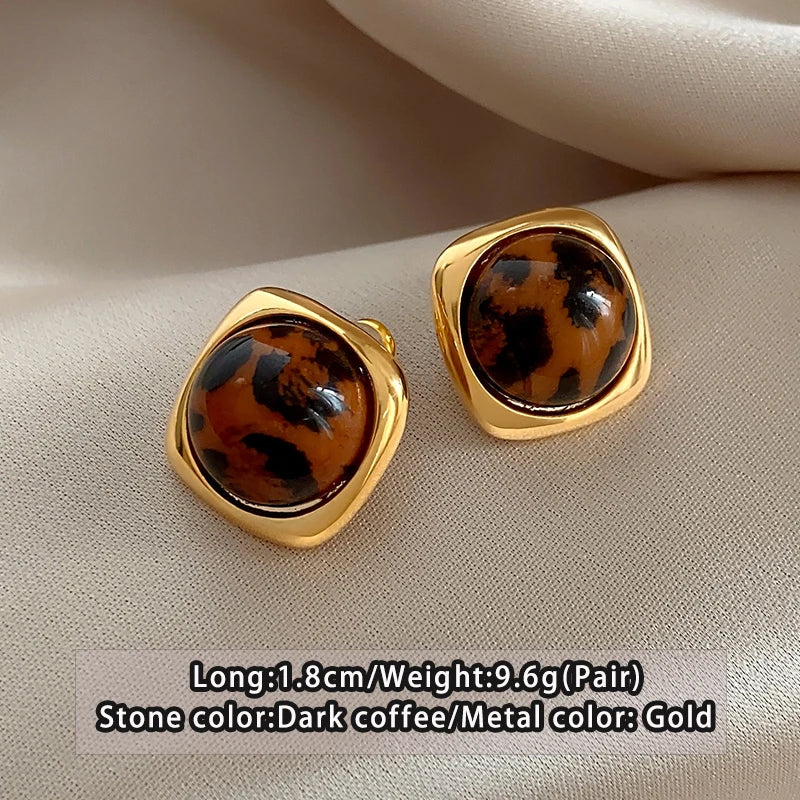 Gold earrings with dark coffee-colored stones on a beige surface