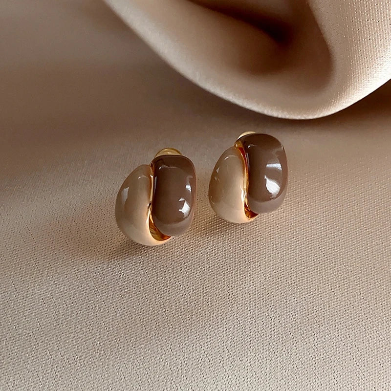 Pair of gold and beige earrings on a beige surface