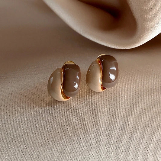 Pair of gold and beige earrings on a beige surface