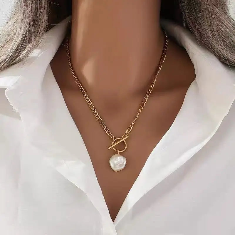 Gold necklace with a pearl pendant worn by a person in a white shirt.