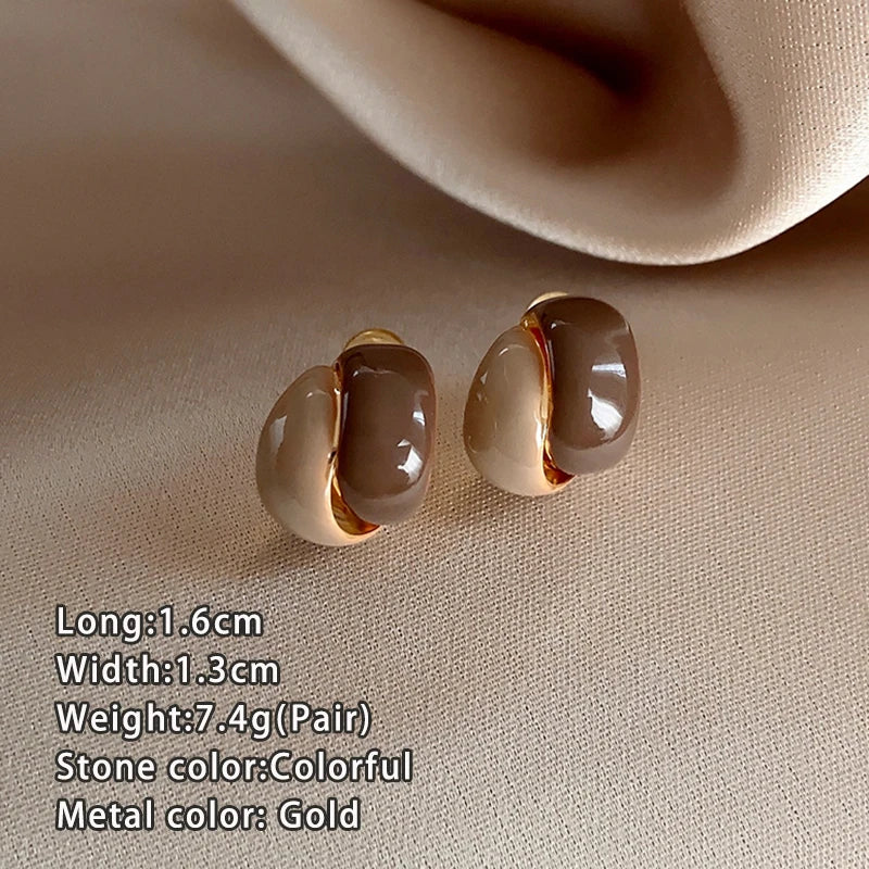 Pair of gold earrings on a beige fabric background with product details.