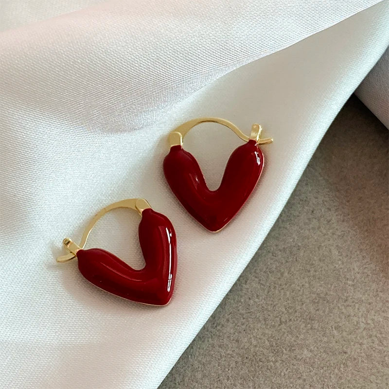 Heart-shaped earrings with gold hoops on a white fabric background