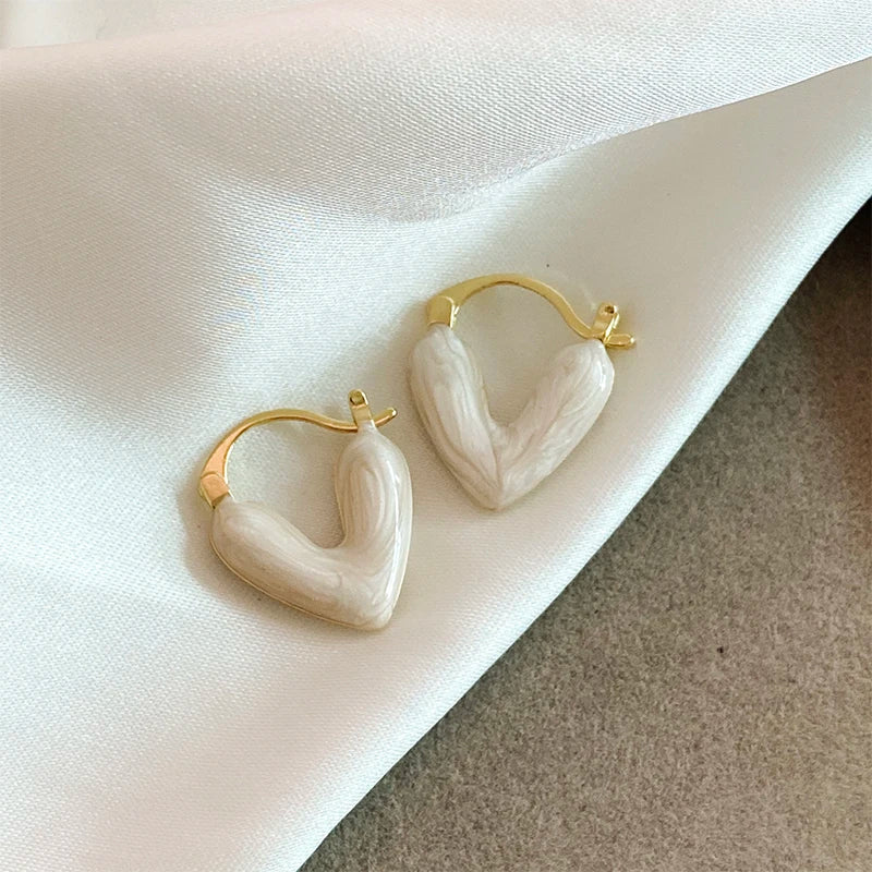Heart-shaped earrings with gold hoops on a white fabric background