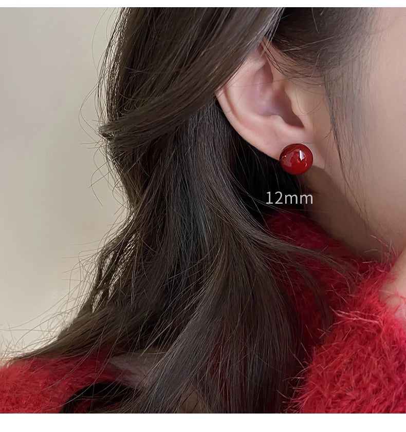 Close-up of a person wearing red earrings with a plain background