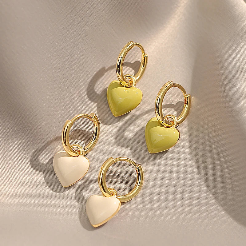 Gold hoop earrings with heart-shaped charms on a beige fabric background
