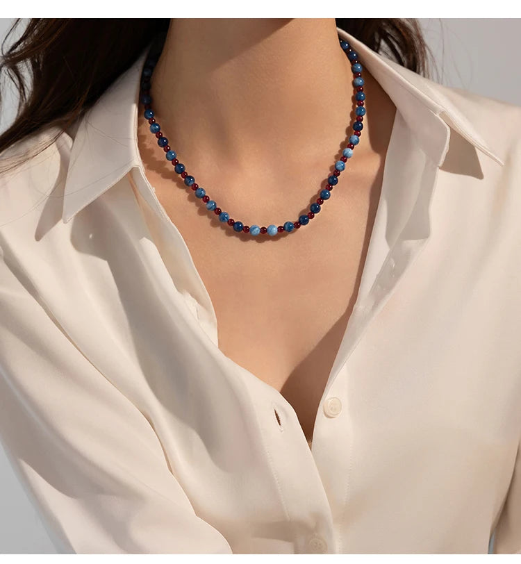 Necklace with blue beads worn by a person wearing a white shirt.