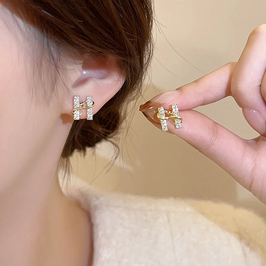 Gold earrings being worn and held up to the ear against a neutral background