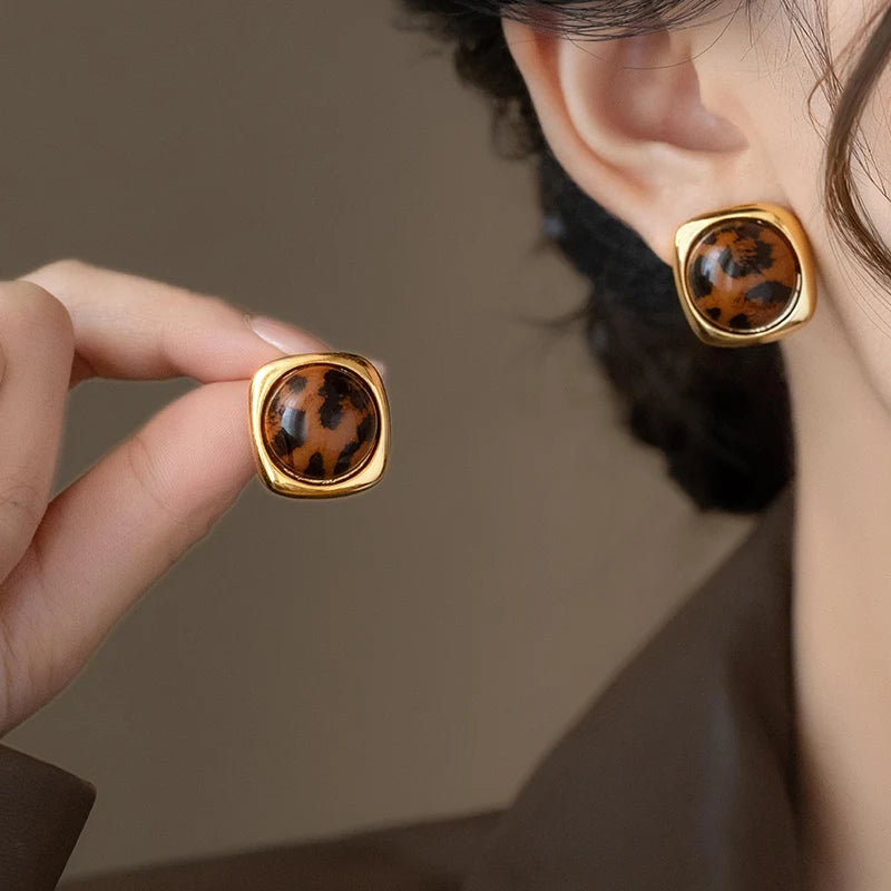 Gold earrings with leopard print stones worn by a person against a neutral background