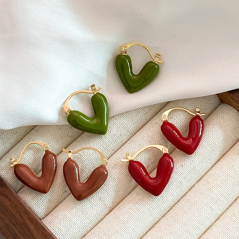 Heart-shaped earrings in green, brown, and red on a textured surface.