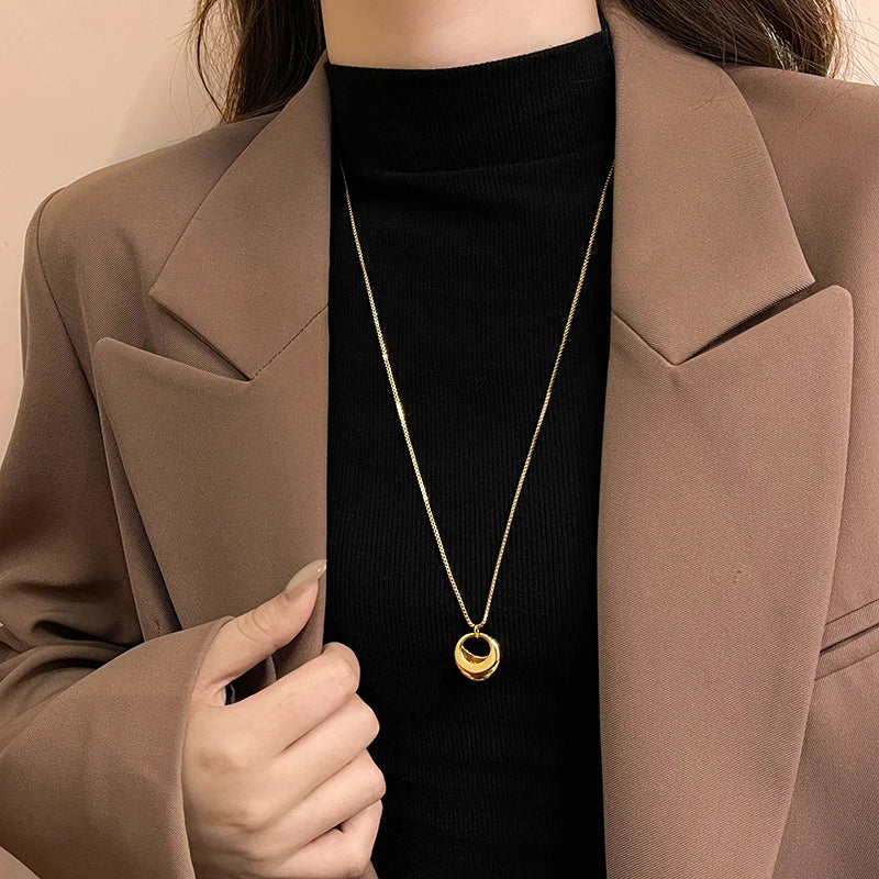 Person wearing a gold necklace with a beige blazer and black turtleneck.