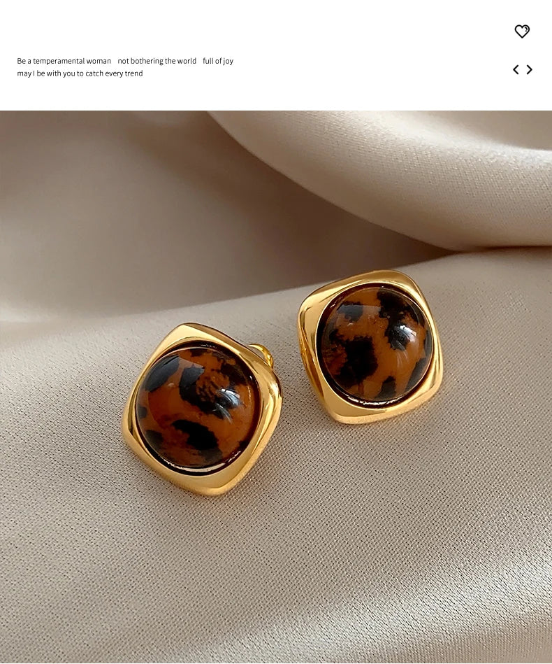 Gold earrings with tortoiseshell design on a beige surface