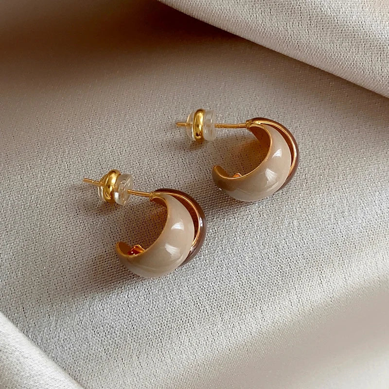 Pair of gold and beige earrings on a textured beige surface
