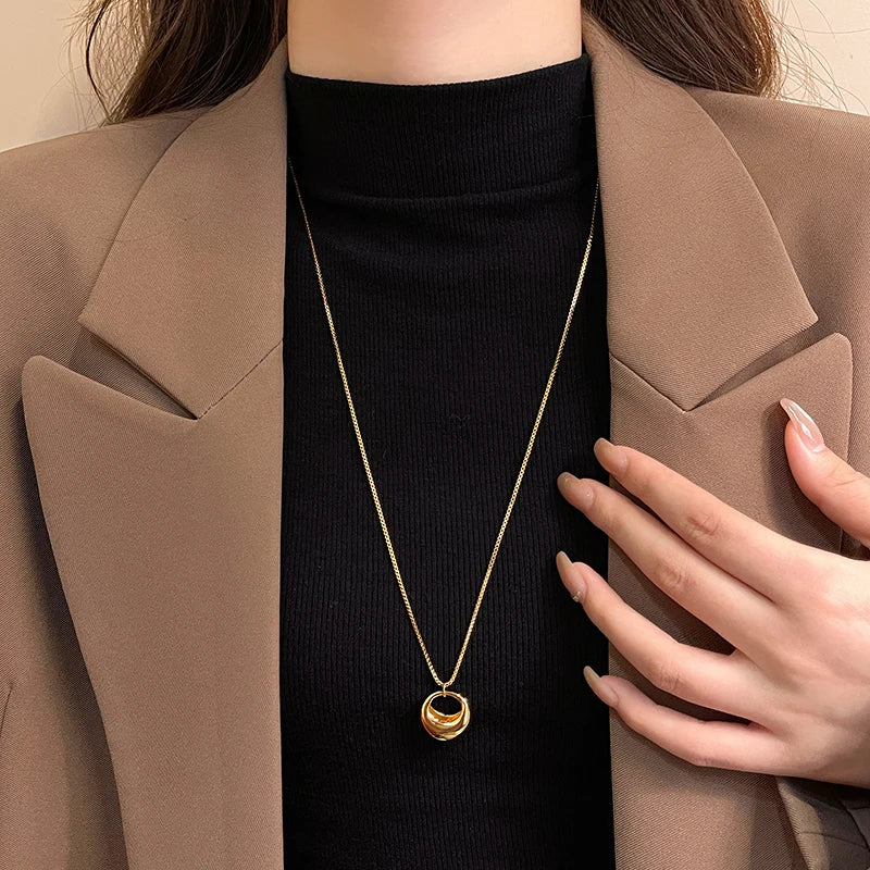 Person wearing a gold necklace with a pendant, holding their hand to their chest.