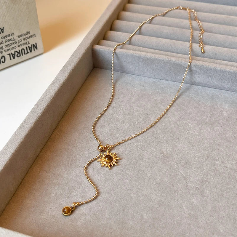 Gold necklace with sun-shaped pendant on a light gray surface