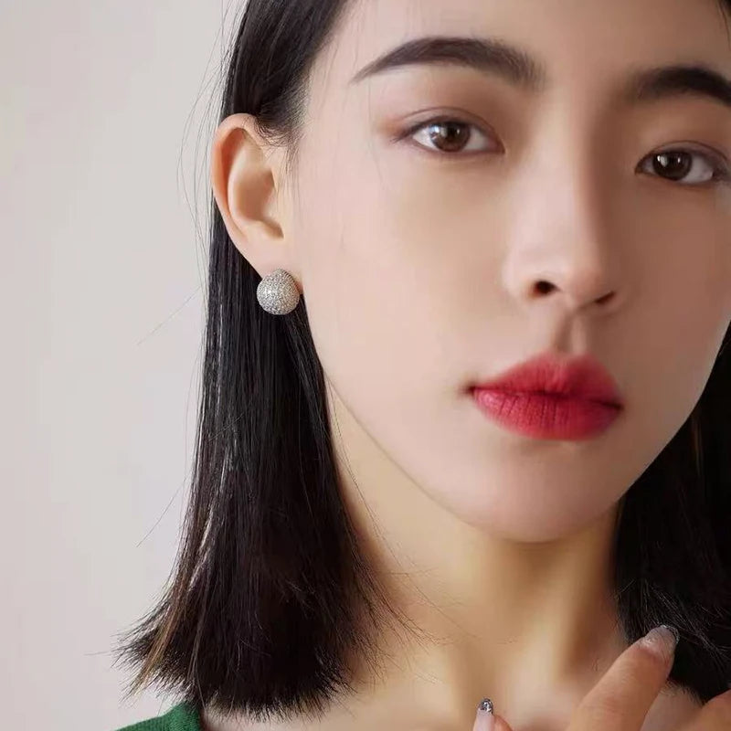 Close-up of a person wearing a pearl earring with a neutral background