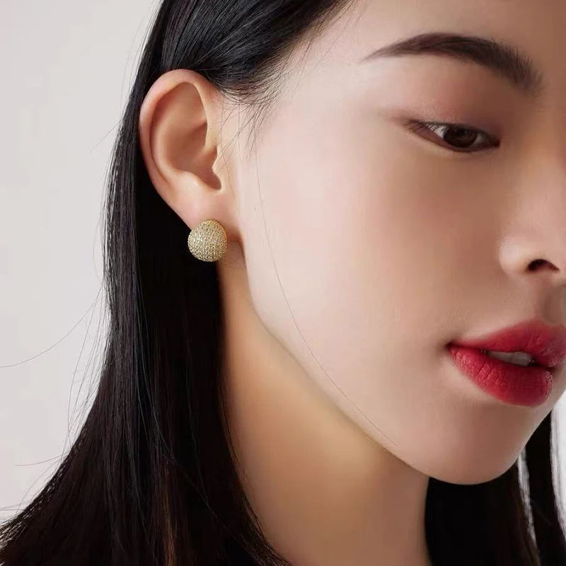 Close-up of a woman wearing gold earrings with a plain background
