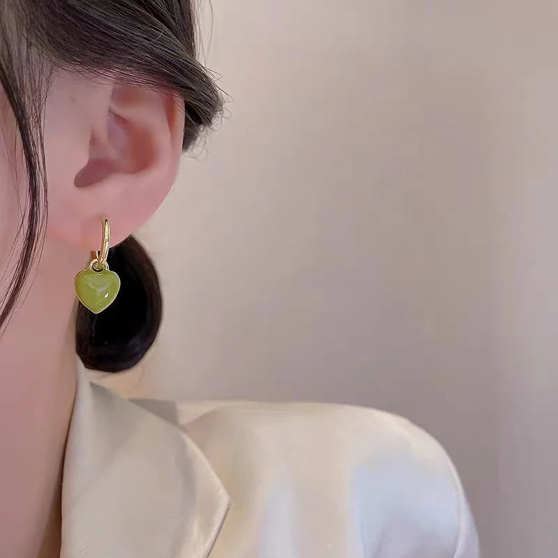 Close-up of an ear wearing a green heart-shaped earring with gold accents.