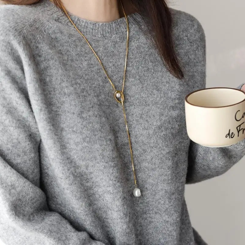 Person wearing a gold necklace with a pendant, holding a mug.