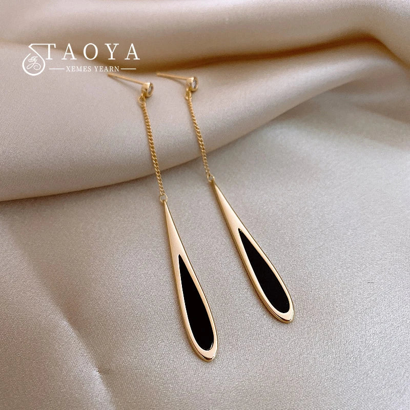 Gold and black earrings on a beige fabric background with 'TAOYA' branding.