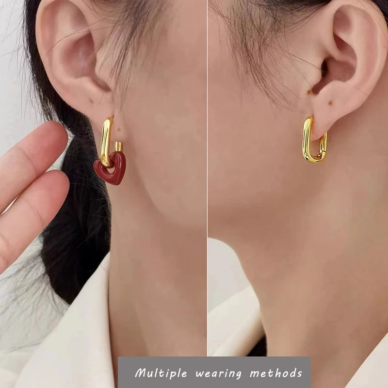 Gold hoop earrings with a red heart detail worn by a person.