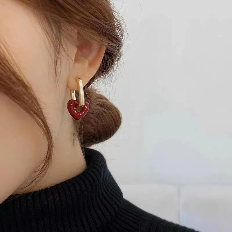 Close-up of an ear wearing a gold hoop earring with a red heart charm against a neutral background.
