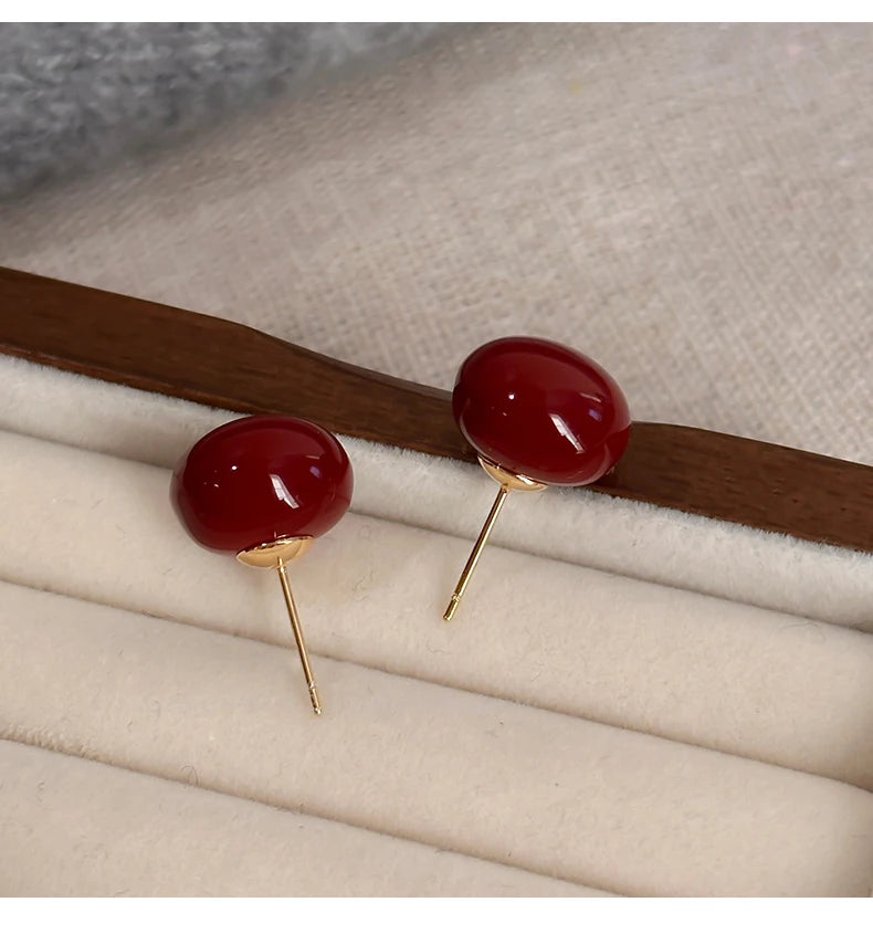 Red earrings with gold posts on a beige surface
