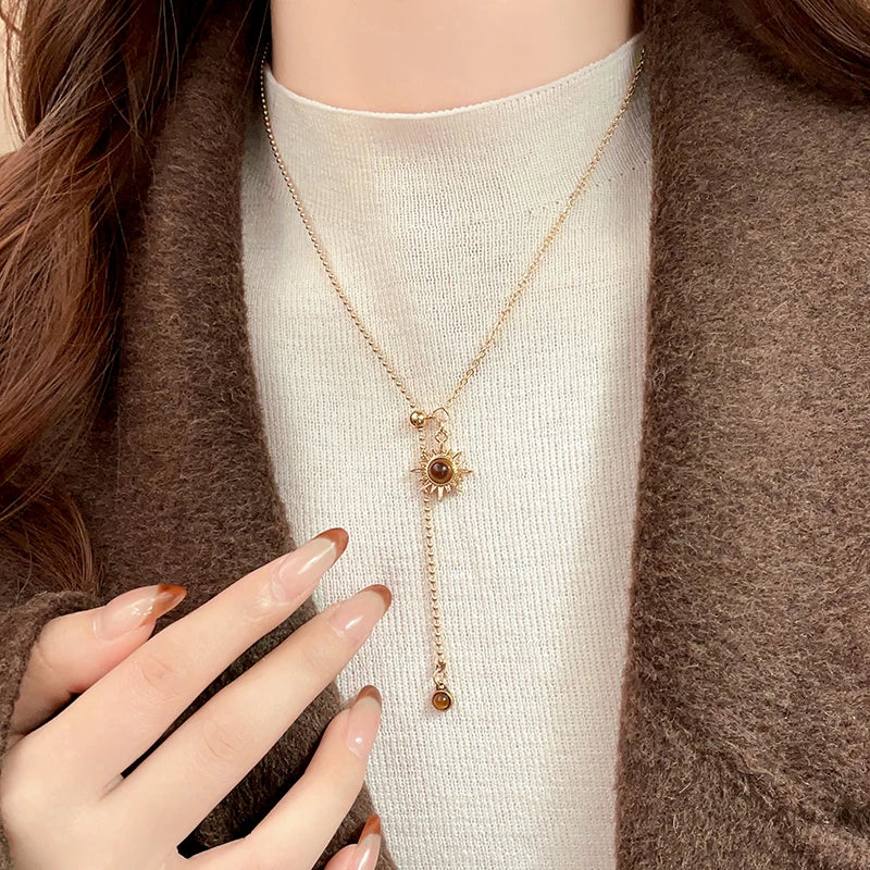 Person wearing a delicate necklace with a sun pendant, set against a neutral background.