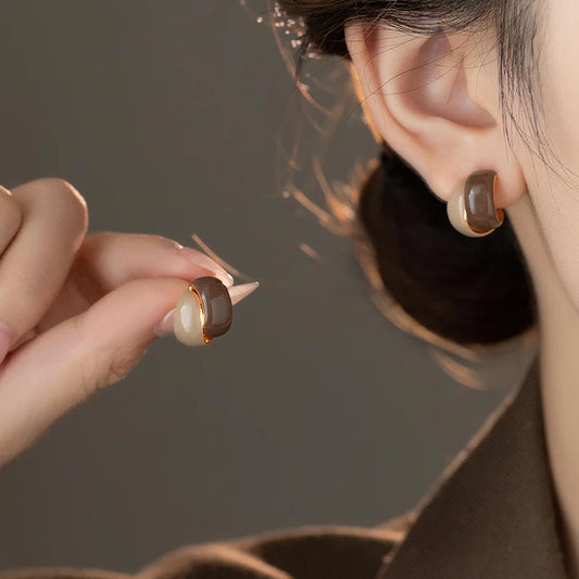 Close-up of an ear wearing a gold and brown earring with a hand holding another similar earring.