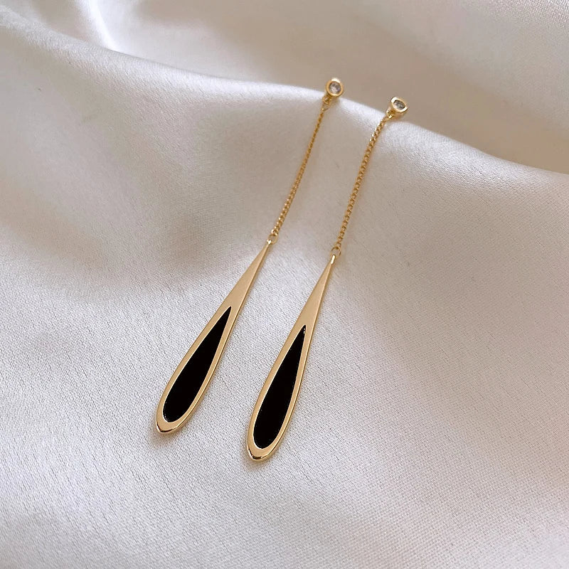 Gold earrings with black oval stones on a beige fabric background