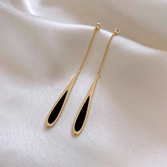 Gold earrings with black oval stones on a beige fabric background