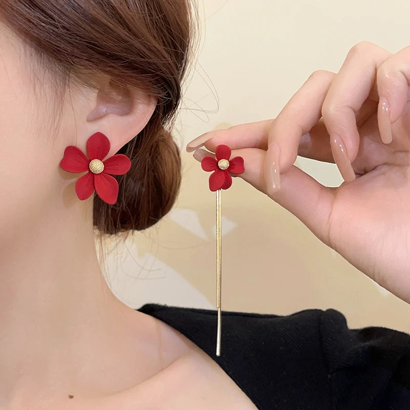 Red flower-shaped earrings being worn and held by a person against a neutral background