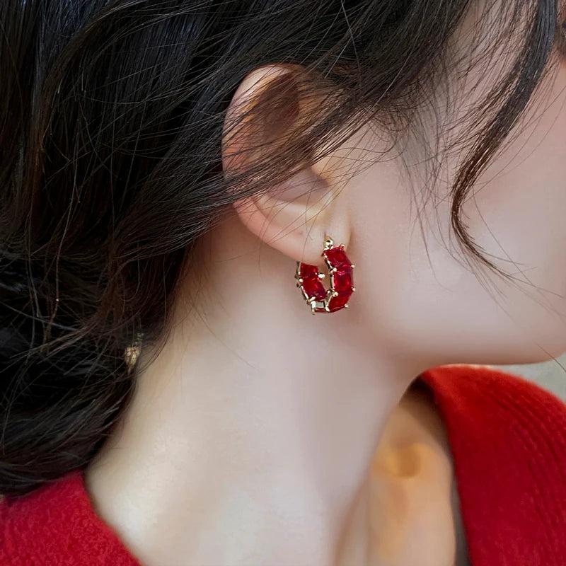 Close-up of a person wearing a red earring with a gold frame.